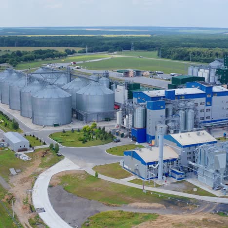 Innovative plant for grain processing. Large complex for agrobusiness on beautiful green landscape. Grain elevators on field. Aerial view