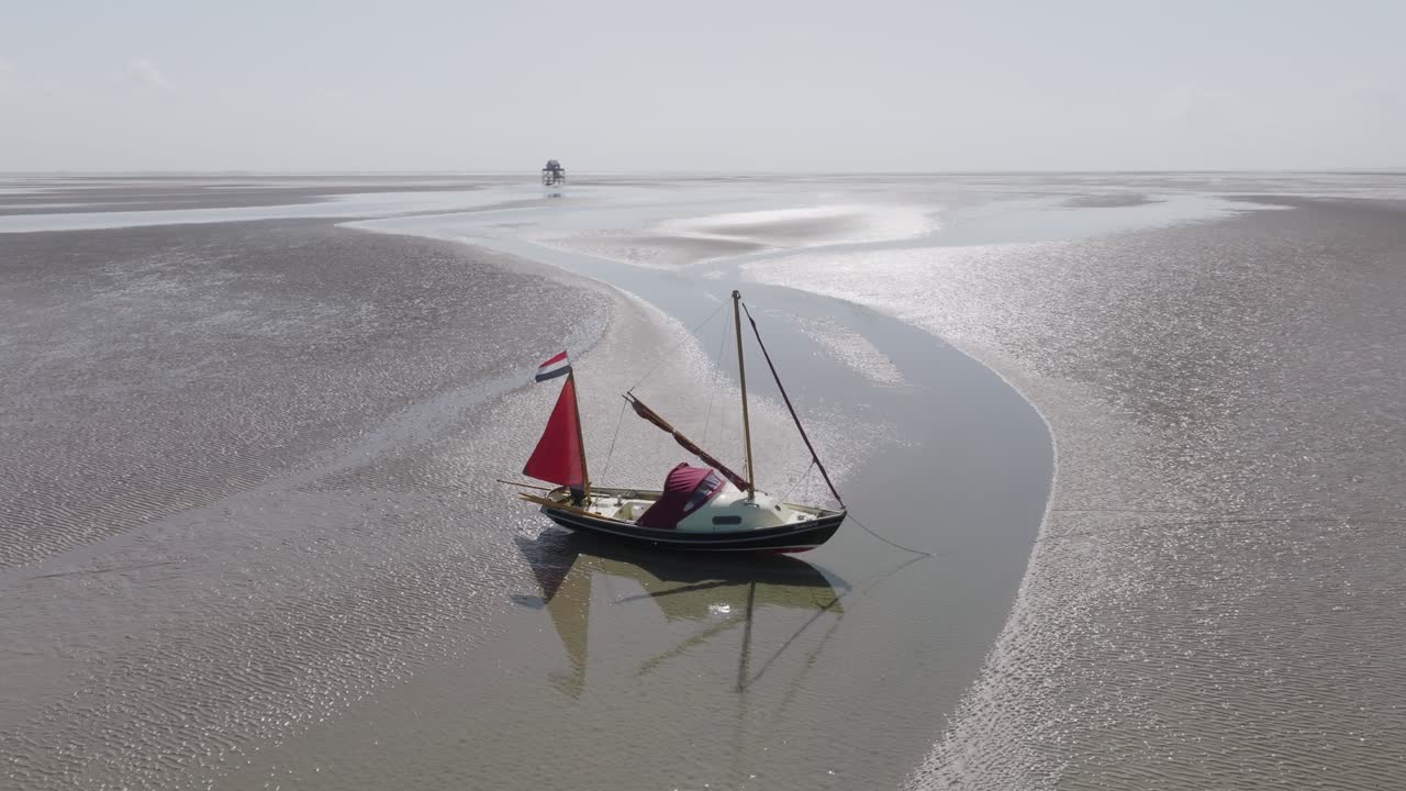 Small sailboat sits aground on Wadden Sea sandbar at low tide; drone at medium altitude performs a slow lateral dolly along the channel and shoreline. Wadden Sea