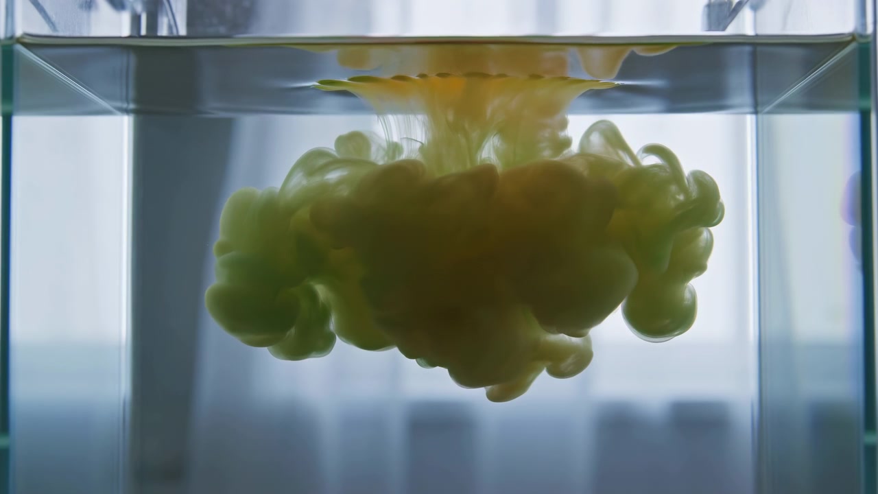 Diffusione di inchiostro verde a metà sequenza all'interno di un serbatoio di vetro trasparente con movimento a pennacchio verso il basso e retroilluminato.