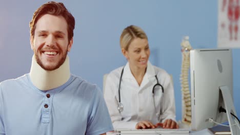 paciente sonriendo a la cámara mientras la fisioterapeuta trabaja en la computadora en el fondo