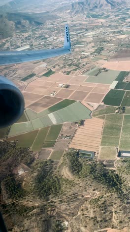 a scenic landscape unfolds through the airplane window, framed by the recognizable ryanair logo on the wing, capturing the essence of mid-flight travel over distant terrain.