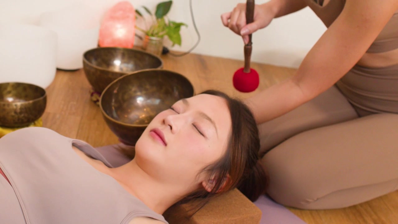 Una donna giace con gli occhi chiusi mentre un terapista usa campane tibetane per la meditazione