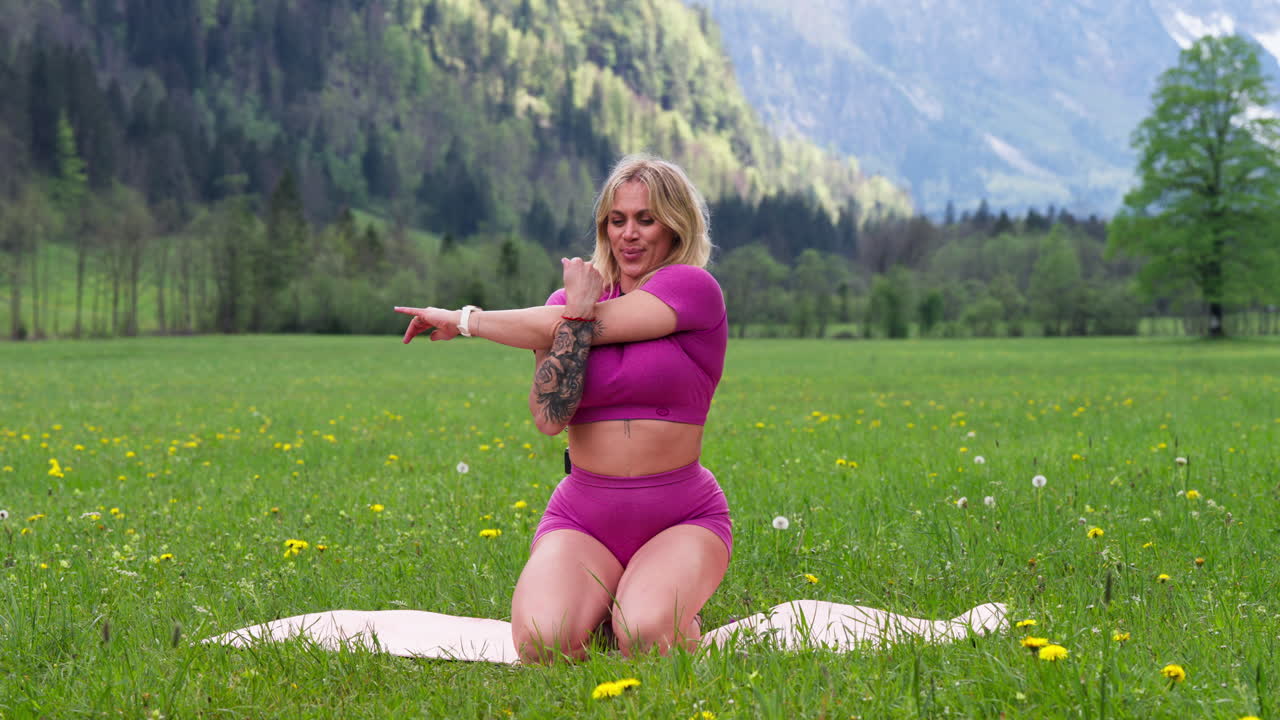 Medium shot of blond woman doing streching and yoga in a green field in the nature, static shot