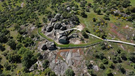 orbital flight with a drone over a viewpoint located on a large granite boat and large rocks around it, fenced in part by a stone wall and has a barbecue area, there are various trees nearby