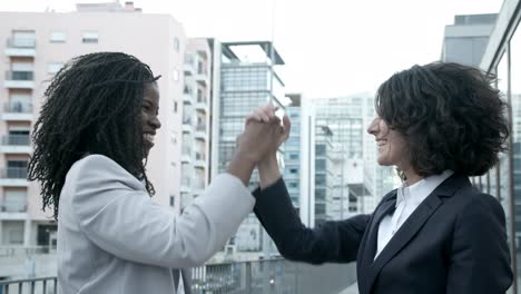 two successful businesswomen shaking hands on street