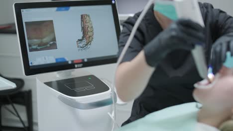 doctor scans the patient's teeth in the clinic. the dentist holds in his hand a manual 3d scanner for the jaw and mouth. dental health. creates a 3d model of teeth and gums on a medical monitor.