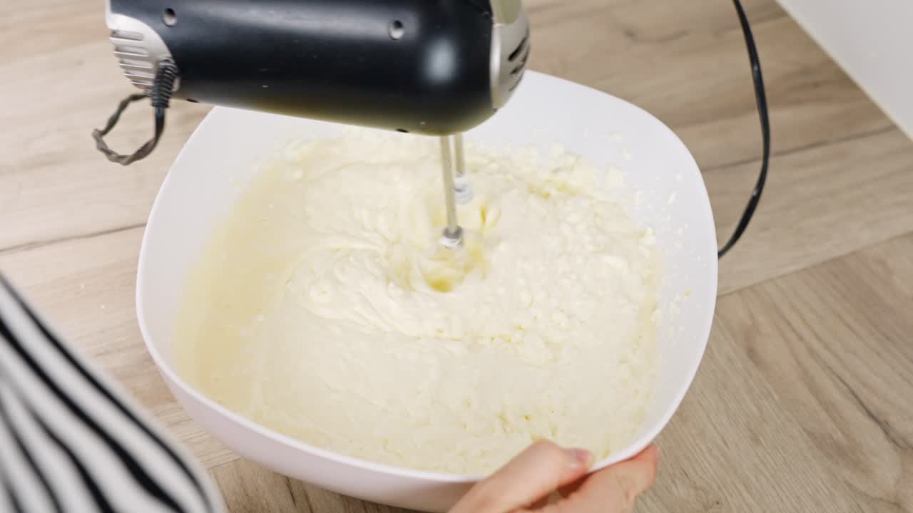Cream is mixed for tiramisu using an electrical mixer, ensuring a smooth and fluffy texture.