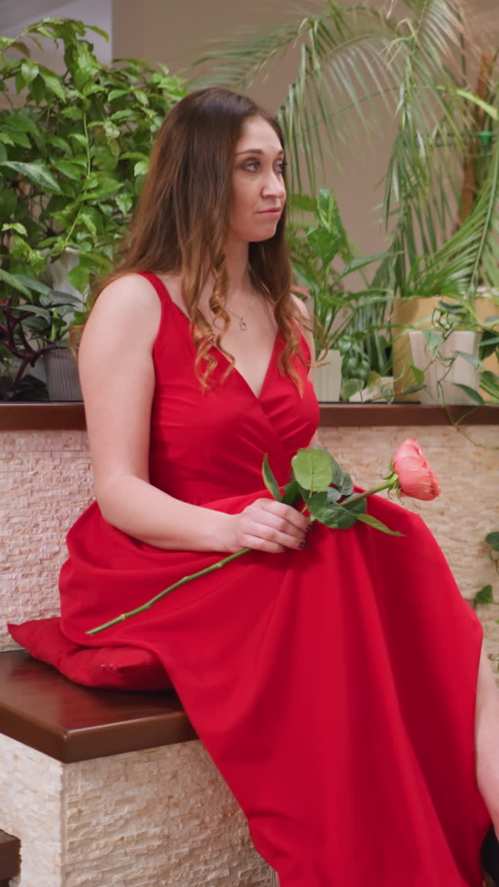Beautiful woman in red dress poses for artist. Attractive young lady holds fresh flower sitting before art master in luxury private house. Live model drawing