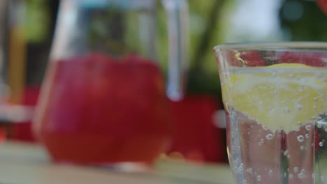 hand pours sparkling drink with lemon into glass, sunlit outdoor setting, shallow depth of field