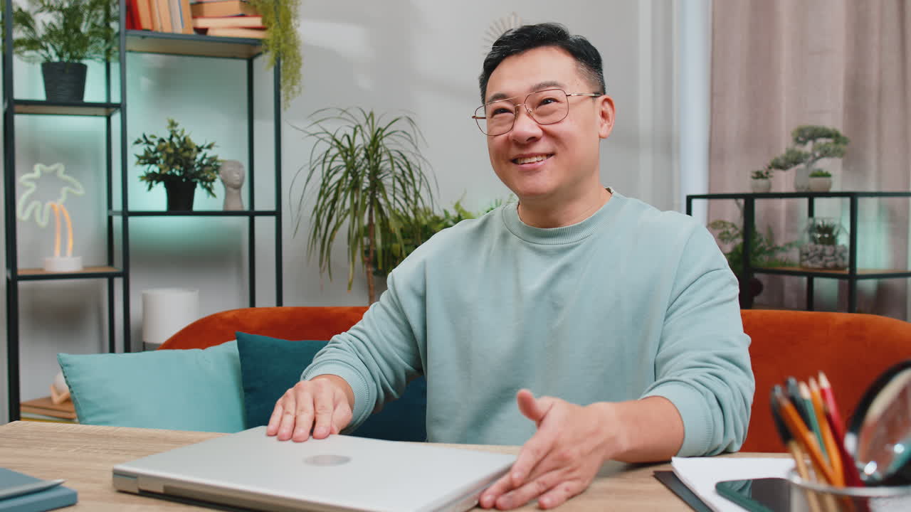 Asian mature man sitting on sofa closing laptop pc after finishing work in living room at home