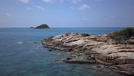 aéreo: un vuelo a baja altitud hacia adelante sobre aguas transparentes azules y una formación rocosa áspera, mar de andamán, tailandia