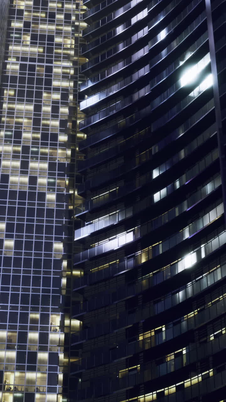 Arranha-céu com fachada de vidro reflexivo brilhando na escuridão da cidade