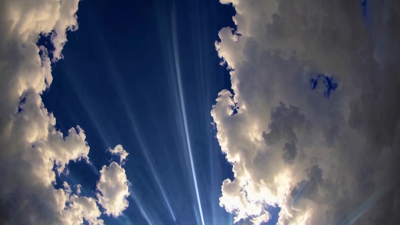 Raggi di sole drammatici che filtrano attraverso le nuvole nel cielo blu
