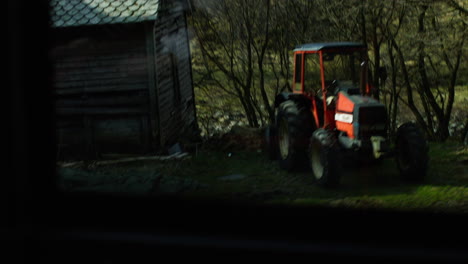 Slow-motion-dolly-shot-past-a-red-tractor-sitting-in-a-field-in-Norway