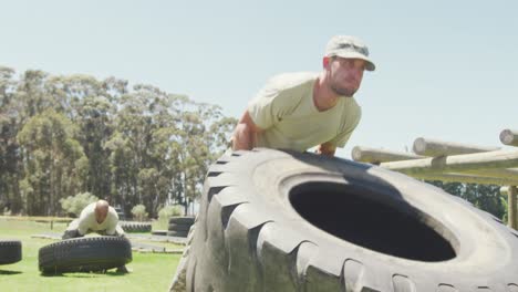 fit caucasian male soldier flipping tractor tyre on army style obstacle course in the sun