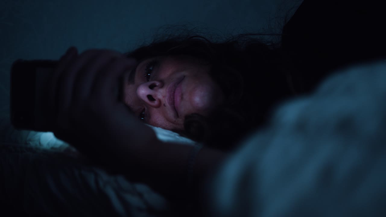 mujer lucha por mantener los ojos abiertos mientras usa un teléfono inteligente en la cama