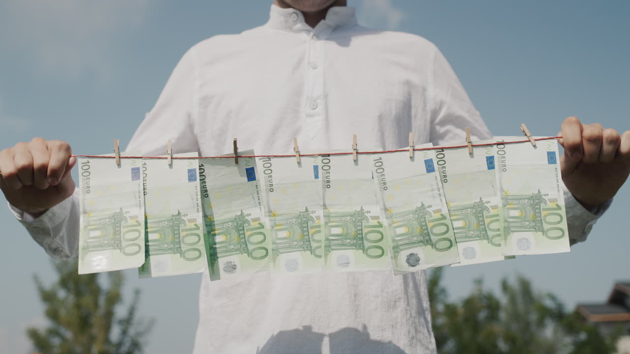한 남자가 손에 옷줄을 들고 있으며, 그 위에 지폐가 매달려 있습니다. 돈세탁 개념. 낮은 각도 촬영