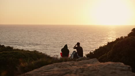 una simple pareja romántica disfrutando de una puesta de sol en el horizonte del mar sentada en rocas