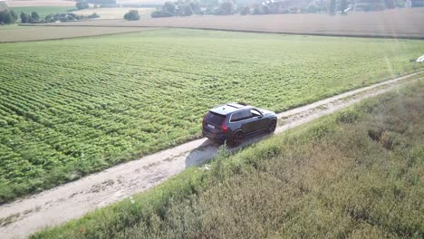 Un-Gran-Coche-Volvo-Conduce-Por-Una-Carretera-Llena-De-Baches-En-La-Campiña-Suiza,-Junto-A-Las-Plantaciones-De-Agricultores,-Suiza,-Vaud