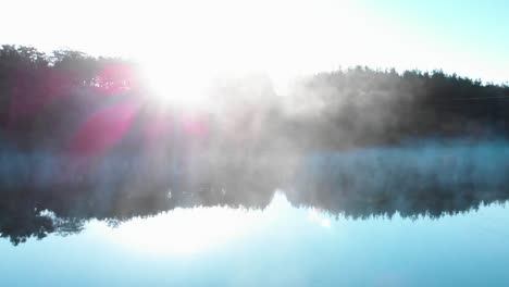 sunrise over forest in front of foggy lake - panning shot