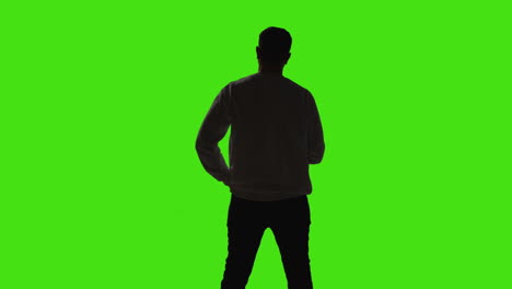 silhouette of man talking on mobile phone standing against green screen with low key lighting from behind