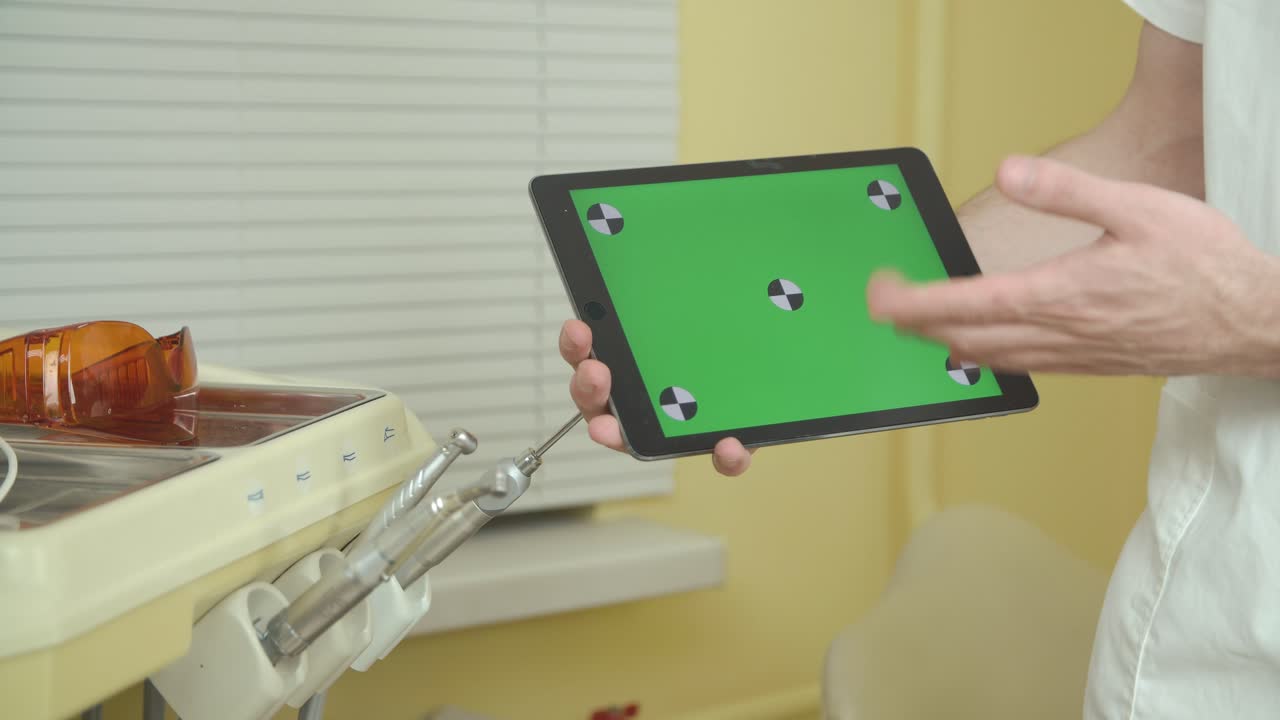 A dentist holding a tablet with a green screen