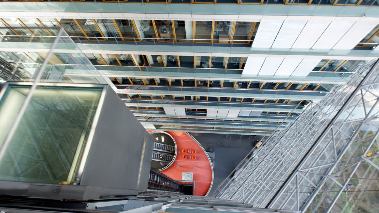 Video from within D&uuml;sseldorf's Stadttor, filmed from above capturing an elevator ascending amidst a vast glass setting, offering a total view of the architectural elegance