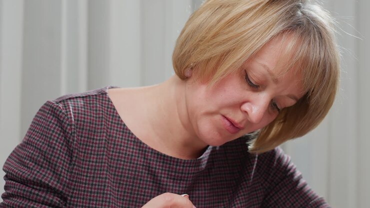 Woman wearing checkered gown and necklace, slightly bent over, focused on her task, she appears busy, engaged in an activity, with a serene expression in a cozy, well-lit environment