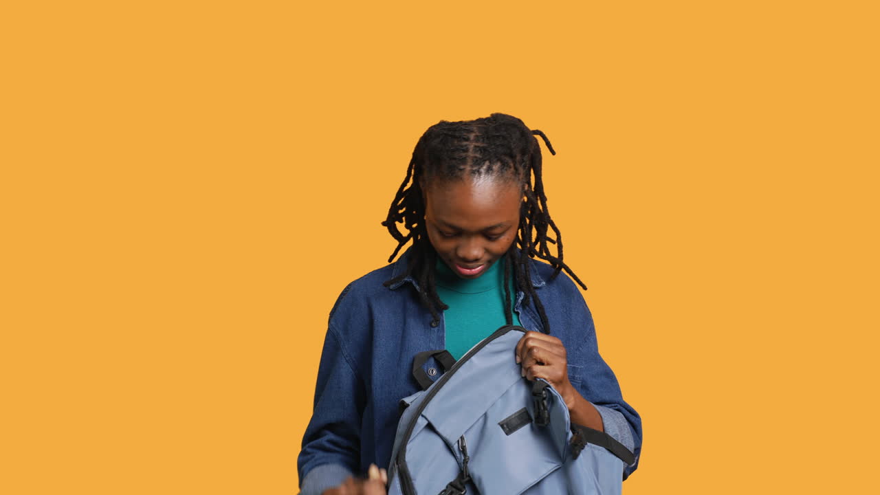 Woman taking laptop out of backpack, preparing to start job, studio background