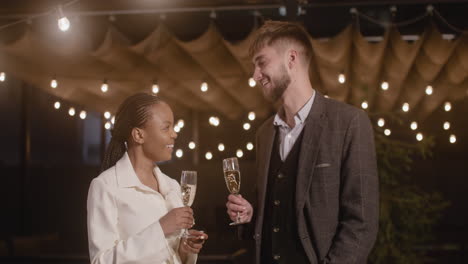 man and woman holding champagne glasses and talking to each other at new year's eve party