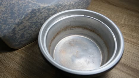 hervidor de arroz vacío y tres tazas de arroz que se vierten en un recipiente de plástico