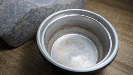 empty rice cooker kettle and three cups of rice being poured into from a plastic container