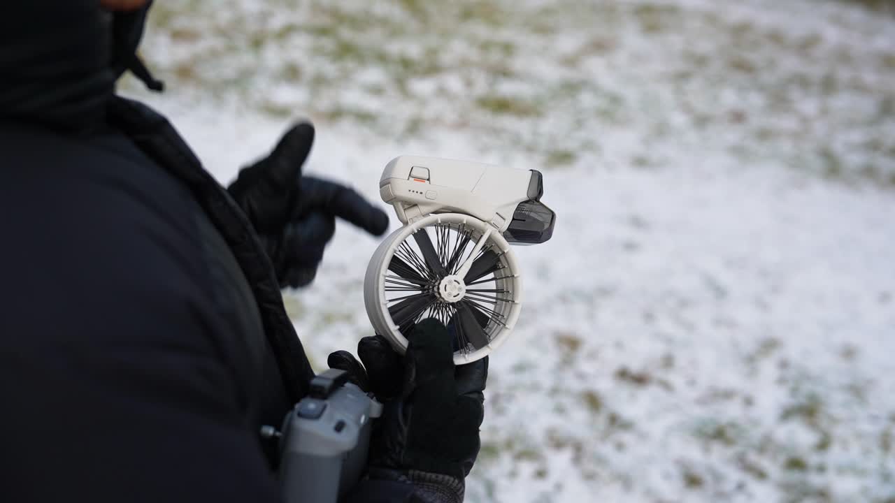 Male inserting battery into drone in snowy winter setting, Czechia