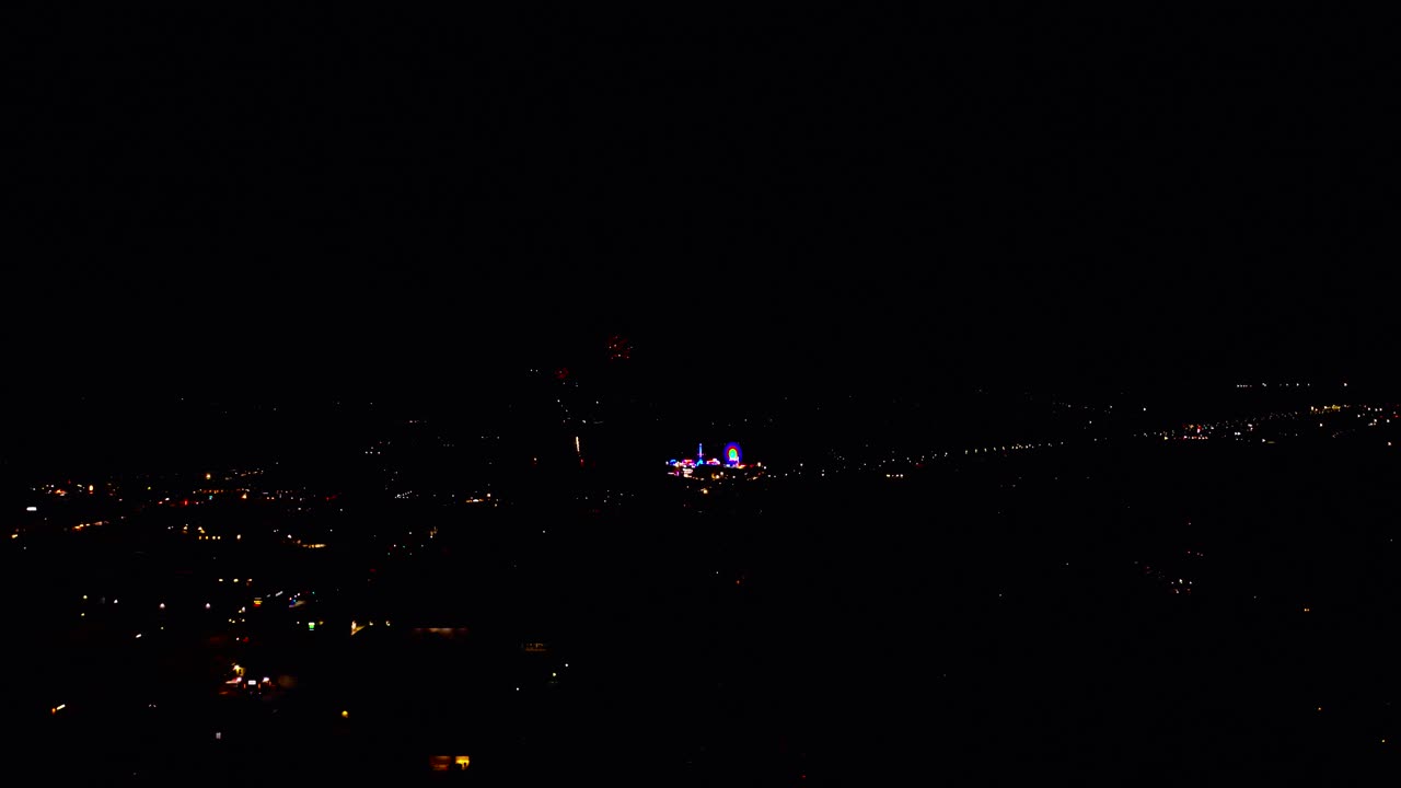 Wide aerial footage of a fireworks display at a county fair in small town at night time in distance
