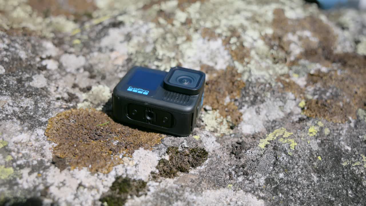 Close-up of an action cameras placed on a rugged, moss-covered rock outdoors.