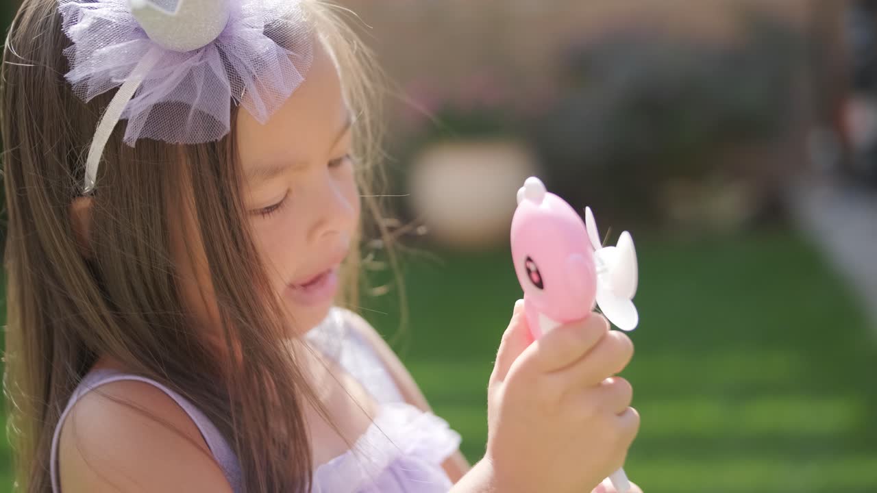 드레스를 입은 작은 소녀가 은 여름날 뒷마당에서 비누 거품을 불고 있습니다.