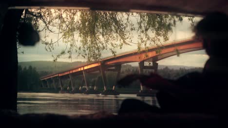 man playing guitar by bridge at sunset