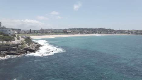 Meereswellen,-Die-Gegen-Die-Felsige-Küste-Von-Bondi-To-Bronte-Küstenwanderung-In-Der-Nähe-Von-Bondi-Icebergs-Pool-Schlagen---Bondi-Beach-Und-Benbuckler-Von-North-Bondi,-Nsw,-Australien