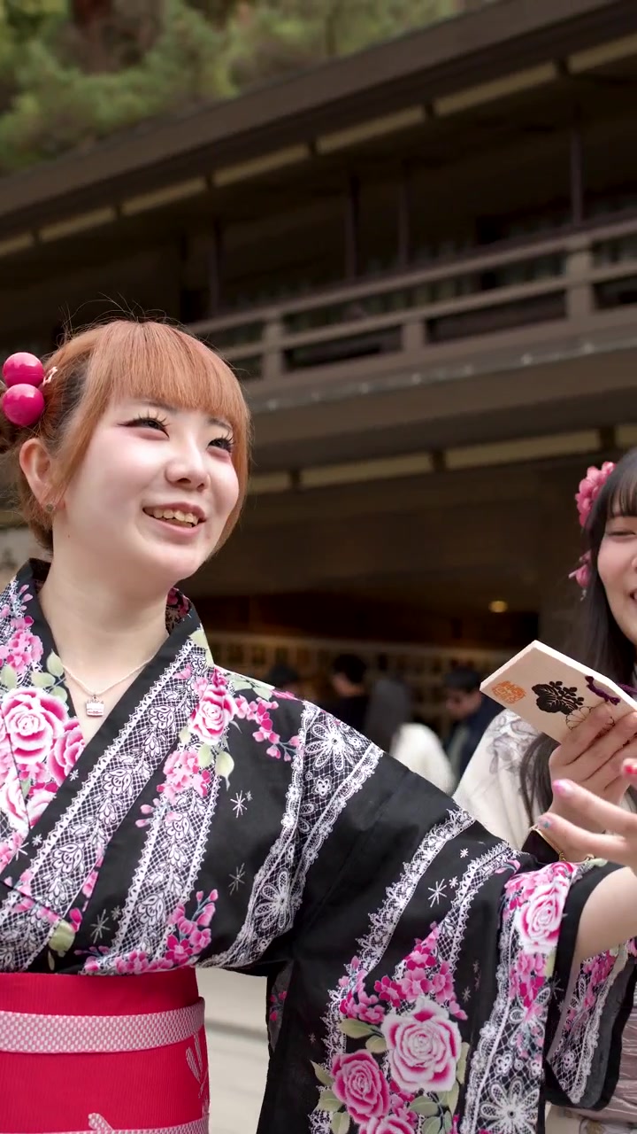Due donne giapponesi sorridenti in kimono tradizionali tengono tavolette votive in legno (ema) in un santuario shintoista.