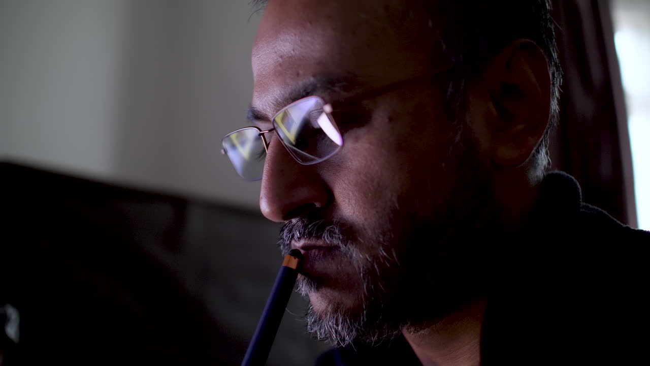 A close up shot of a South Asian man with a pen on his lips deep in thought