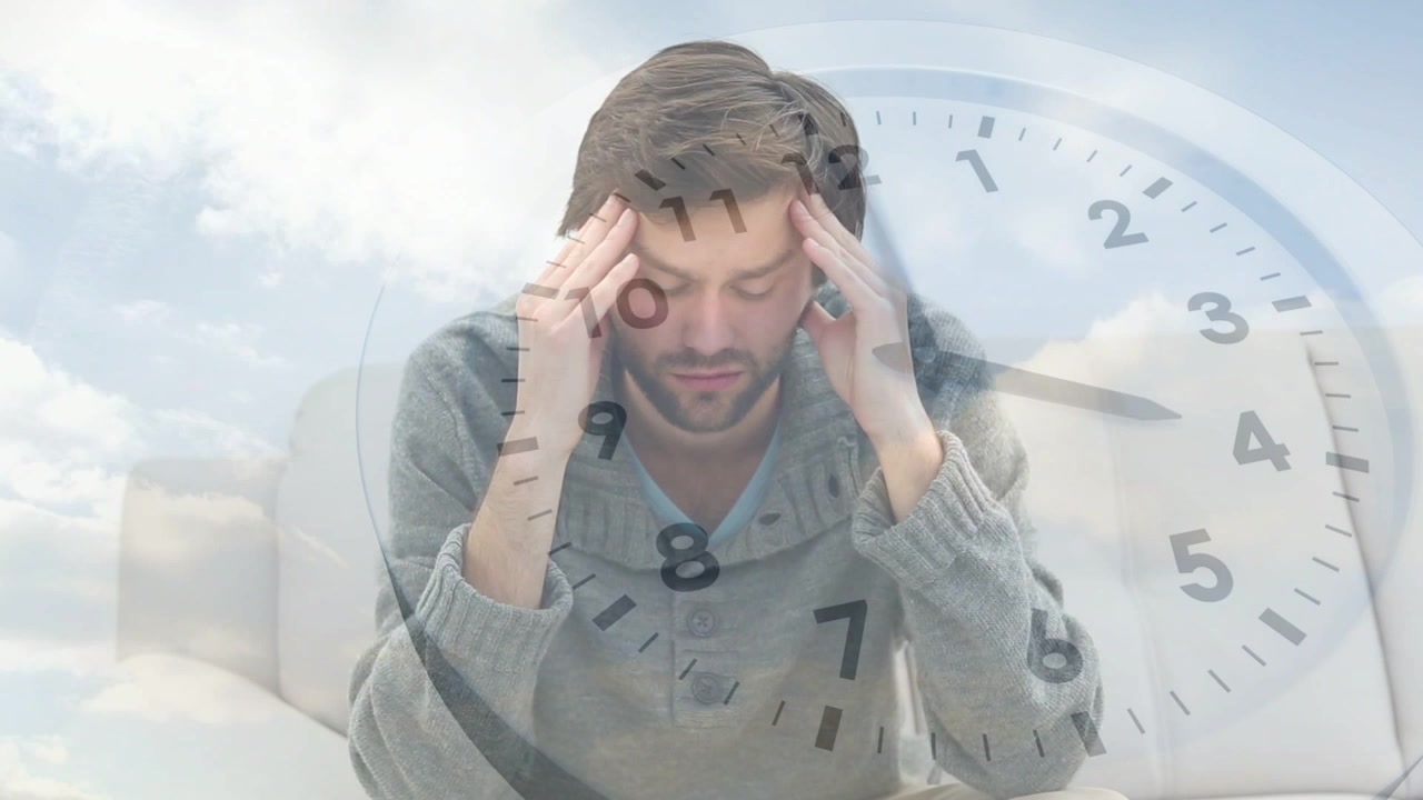Uomo seduto sul divano che si strofina le tempie mentre appare un'icona di orologio in sovrimpressione, segnalando stress per la salute legato al tempo.