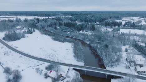 abava river winding through a snowy landscape near renda village , winter setting, aerial view, moving backward, tilt down