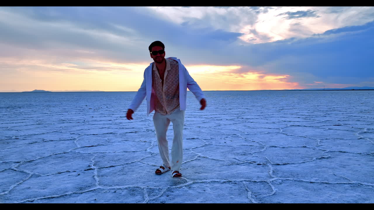 Joyful man wearing sunglasses dances cheerfully in front camera. Man steps crusty salty landscape in Bonneville Salt Flats, Utah, USA