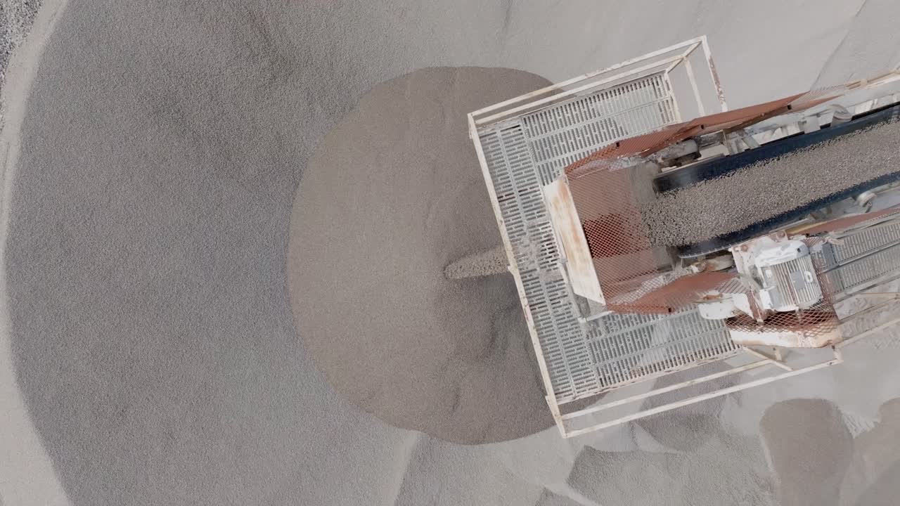 Top down close up aerial footage of small rocks going to the end of a conveyor belt and falling off into a large pile.
