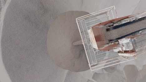top down close up aerial footage of small rocks going to the end of a conveyor belt and falling off into a large pile.