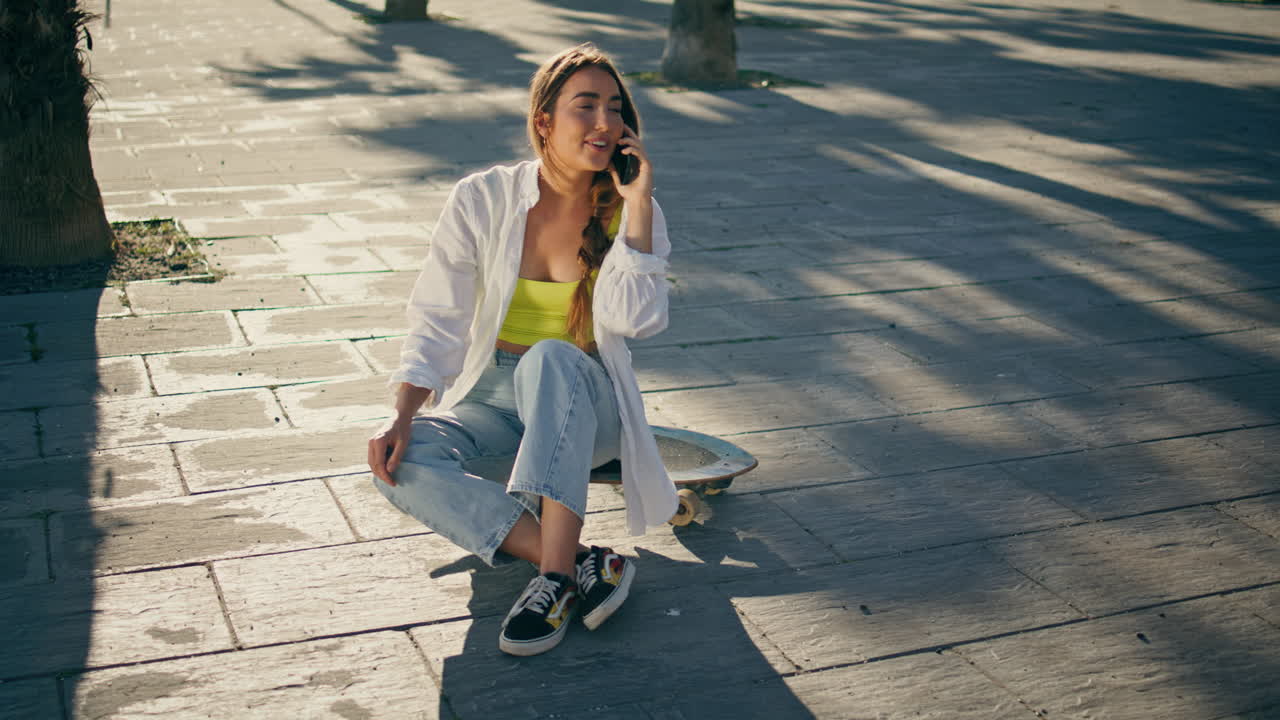 patinador amistoso hablando teléfono inteligente en la avenida soleada. mujer hablando teléfono móvil