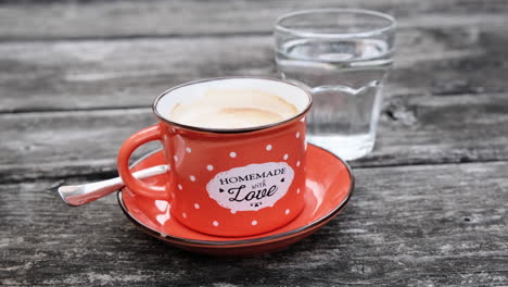 homemade coffee in red enamel cup on rustic wooden table with a glass of water