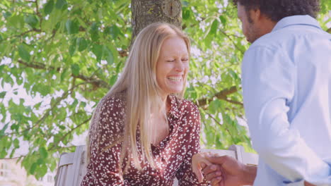 Romantic-Mature-Man-Proposing-To-Surprised-Woman-Sitting-On-Park-Bench-With-Engagement-Ring-In-Box