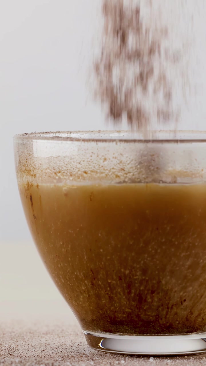 Primo piano di polvere di caffè che si dissolve in una tazza di vetro con acqua calda e illuminazione soffusa.