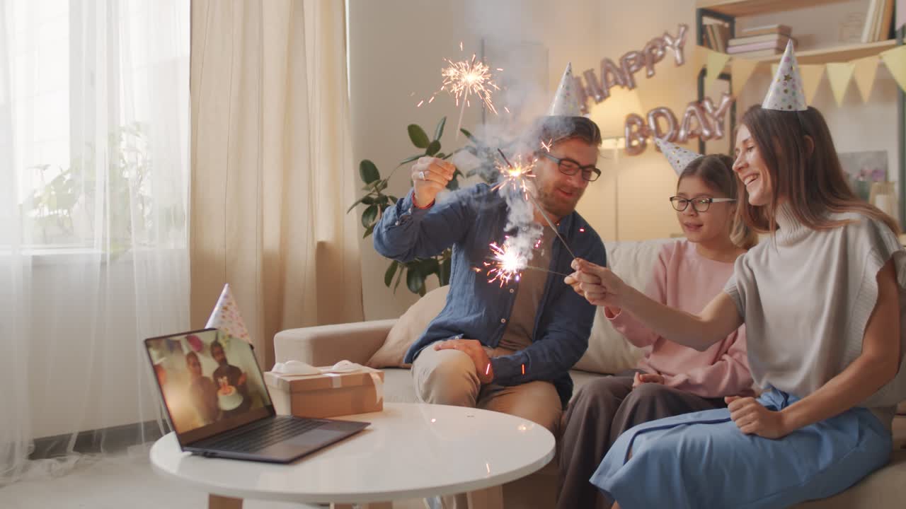 padres e hija celebrando cumpleaños en línea con sombreros de cumpleaños y destellos que agitan